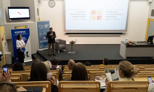 Widok na salę wykładową z uczestnikami siedzącymi w ławkach. Na scenie Rektor otwiera konferencję, za nim znajduje się duży ekran z tytułem konferencji &bdquo;Wyzwania wsp&oacute;łczesnego publikowania&rdquo;.